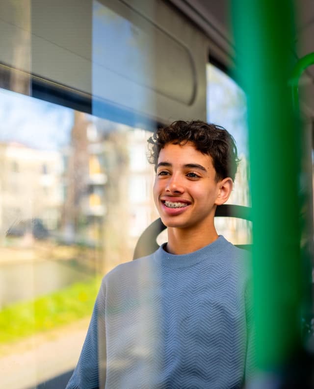 Jonge jongen met donker haar zit glimlachend in de bus aan de kant van het raam